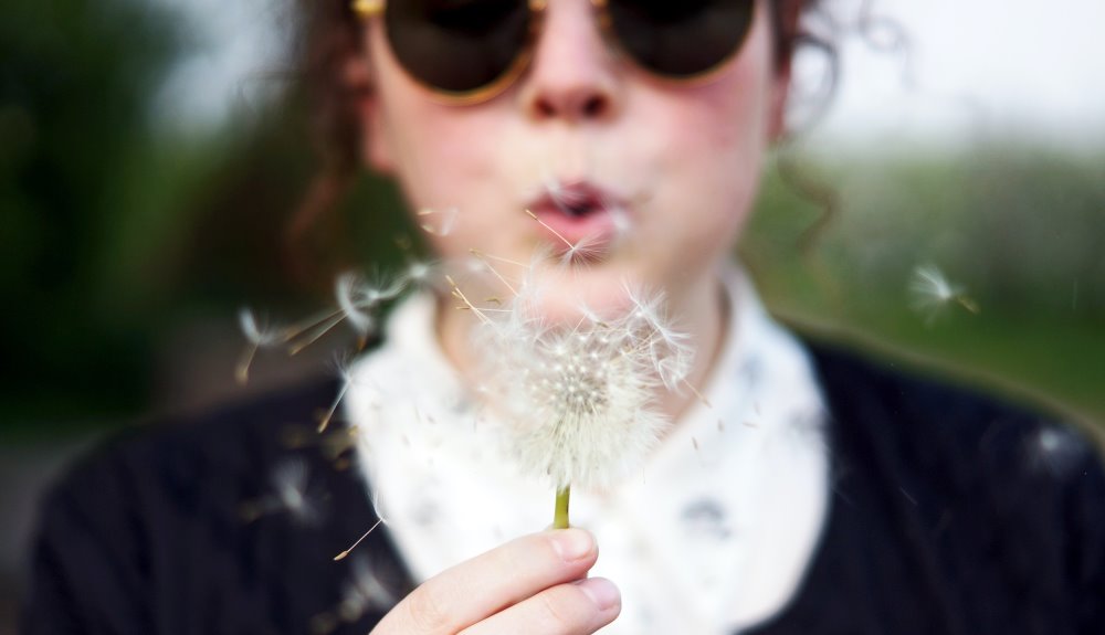 girl blowing on dandelion